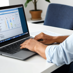 A calm and focused professional, fully clothed in a modest smart casual outfit, sitting at a modern desk in a well-lit home office. They are looking confidently at a laptop screen, which subtly displays elements related to financial planning or savings, representing economic benefit. The background shows a neat, professional home environment. Perfect anatomy, correct proportions, natural pose, well-formed hands, proper finger count, natural body proportions. Professional photography, high quality, safe for work, appropriate content, family-friendly.